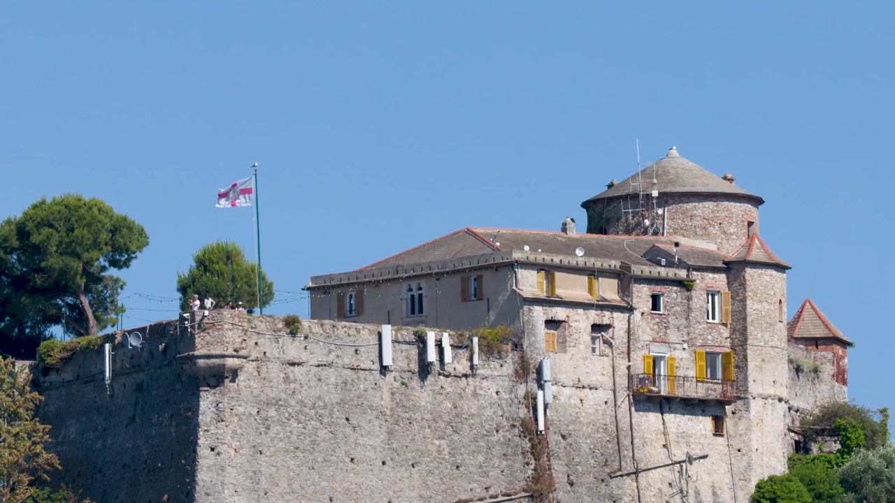 Ampia inquadratura fissa di un castello storico in pietra con torri e bandiere sotto un sole splendente
