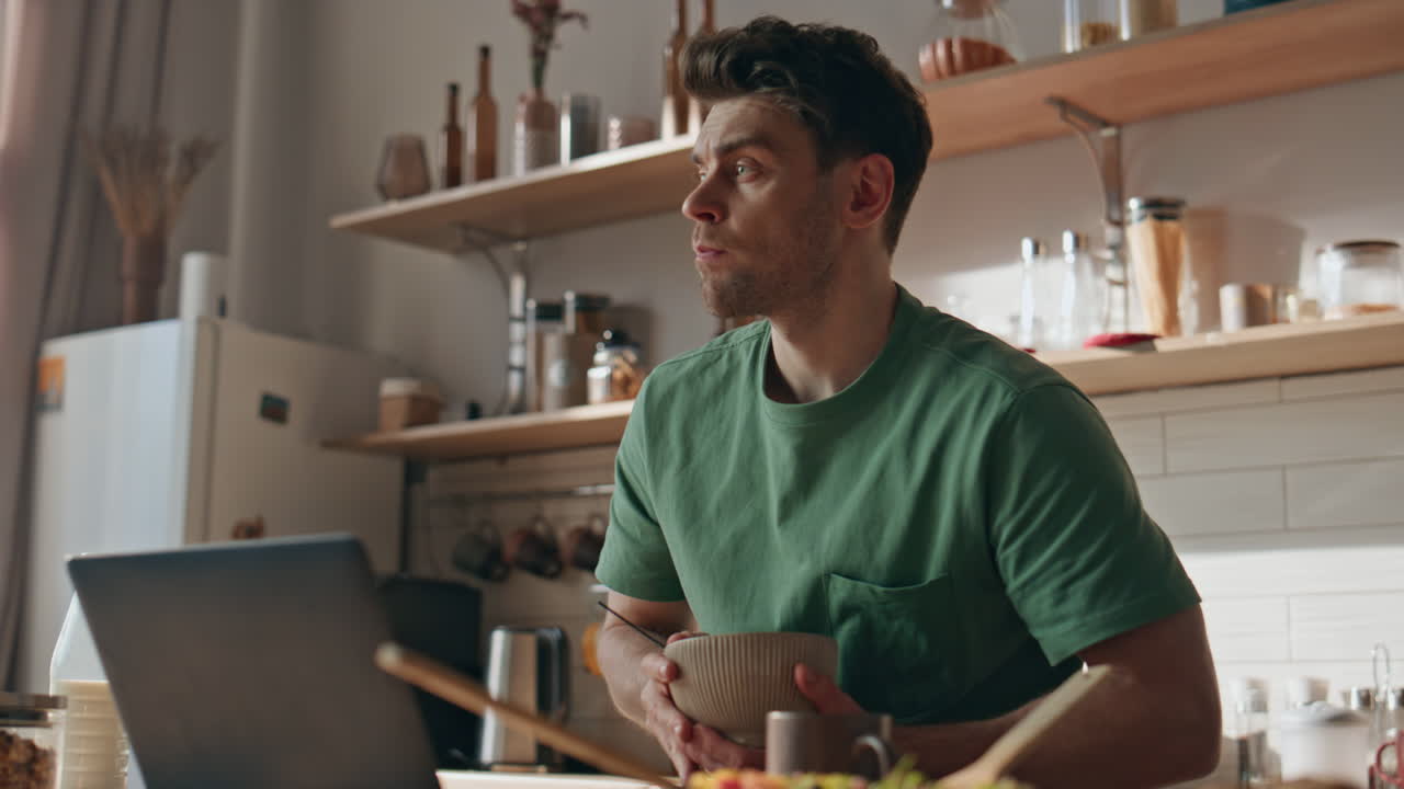 Focused man having breakfast reading laptop kitchen closeup. Guy eating granola