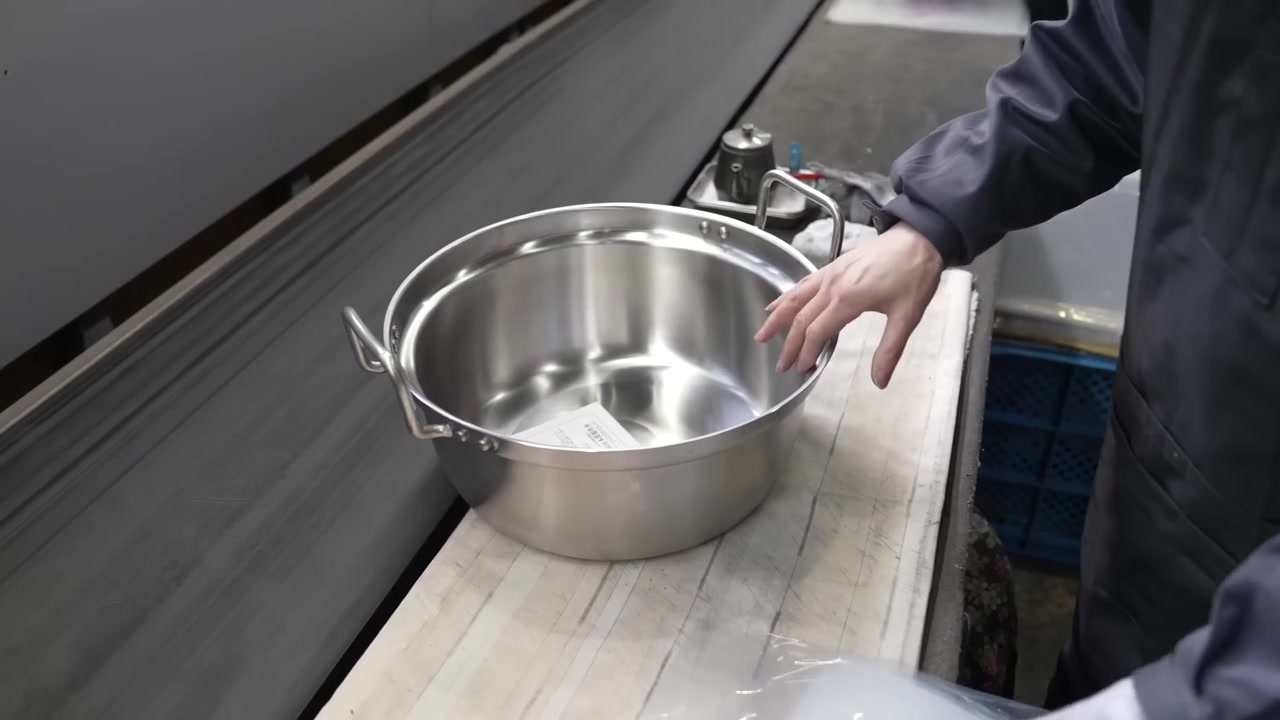 Worker inspecting polished stainless steel pot and putting it in plastic bag for packing