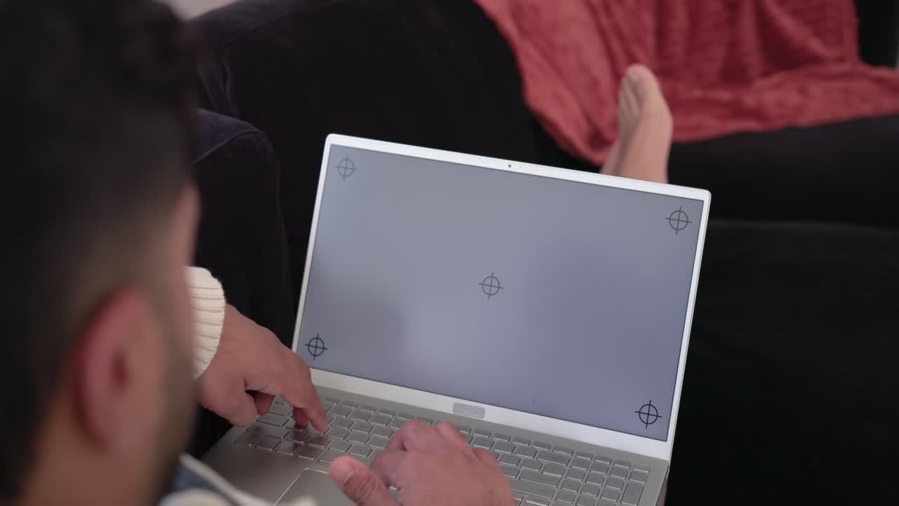 Man is typing on laptop on couch after placing hands while companion's feet are resting