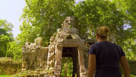 rear view of female caucasian tourist walking towards smiling buddha tower in angkor, siem reap, cambodia