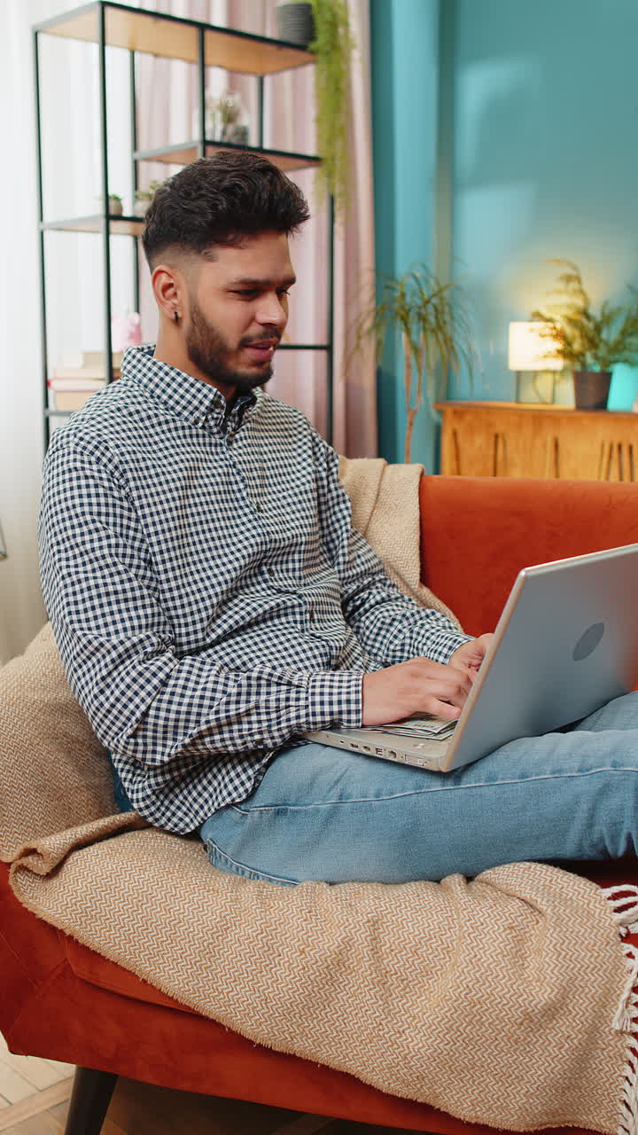 Indian happy man counting money cash and use laptop pc calculate domestic income earnings at home