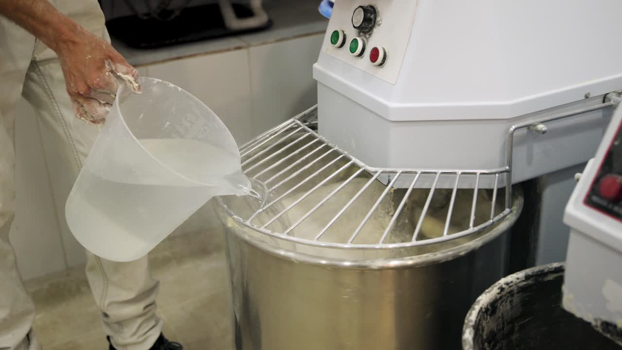 Baker Adding Water to Industrial Dough Mixer in Commercial Kitchen