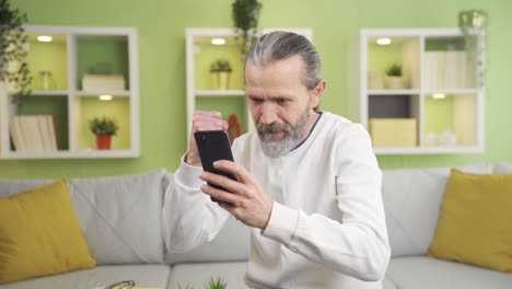 el anciano mirando el teléfono inteligente en casa se alegra, gana, alegría de buenas noticias.