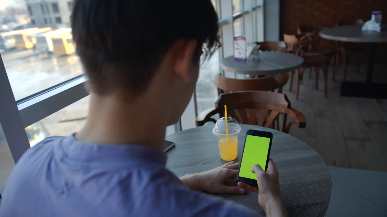 cámara portátil: punto de vista de un hombre en un café moderno sentado en una silla usando un teléfono con pantalla de maqueta verde tecla de croma navegando por internet viendo vídeos de contenido blogs tocando en la pantalla central