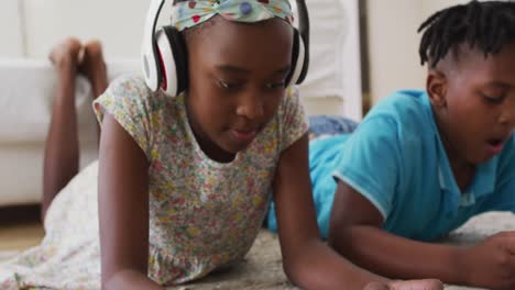 african american brother and sister using electronic devices lying on the floor at home