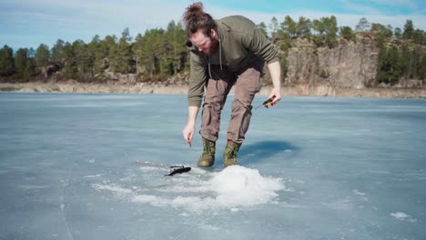 man pulling the fishing rod line with catch fish on frozen lake