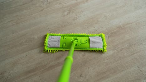 cleaning the house. green microfiber mop moving on the parquet floor to keep the house clean. housekeeping concept. close-up.