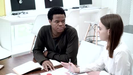 medium shot of female college student helping her friend with difficult assignment. african american boy and caucasian girl sitting at desk and discussing task