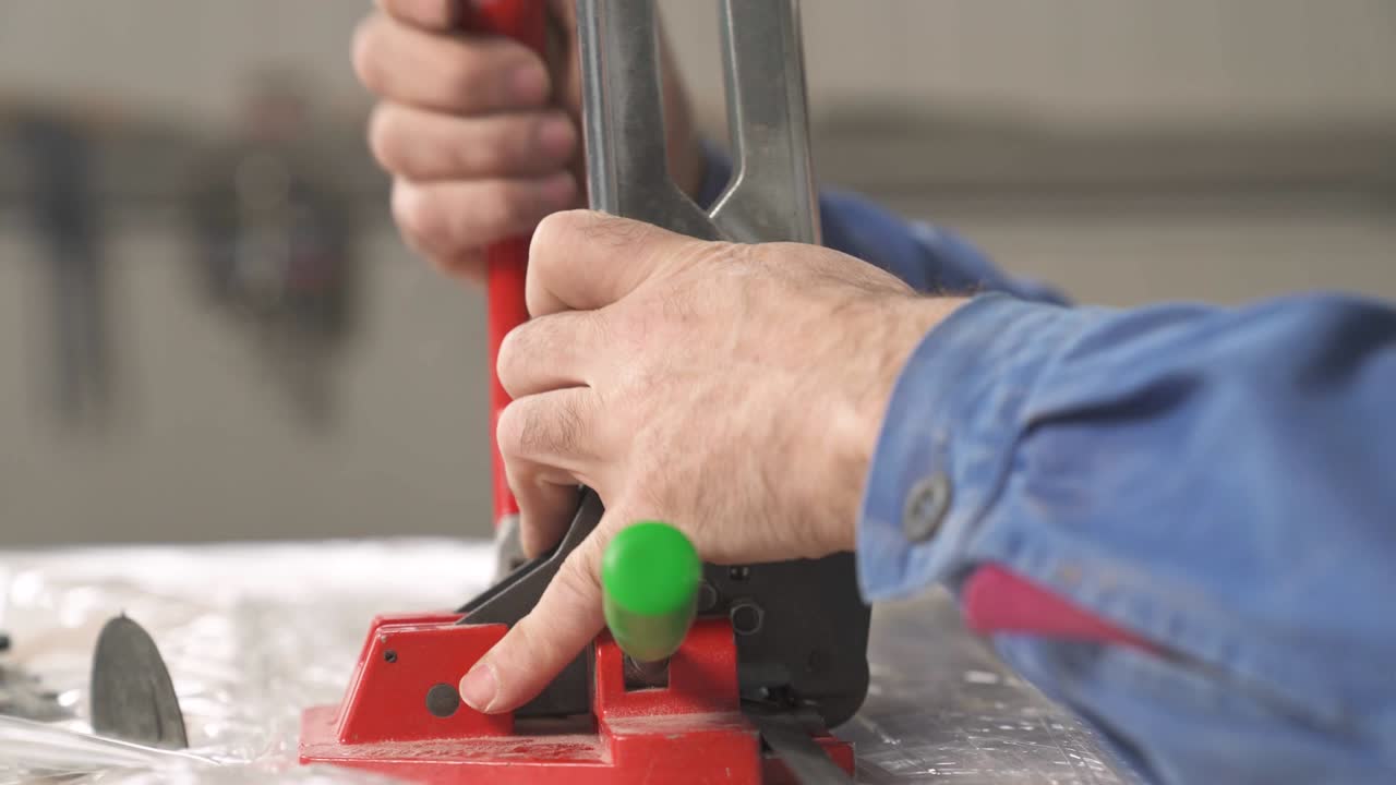 un primer plano de una mano de trabajador uniendo con un equipo especial los extremos de una cuerda de envoltura de plástico para empacar briquetas de madera