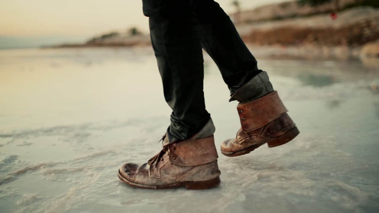 hombre con viejas botas de cuero sucias caminando por la orilla salada del mar muerto, israel