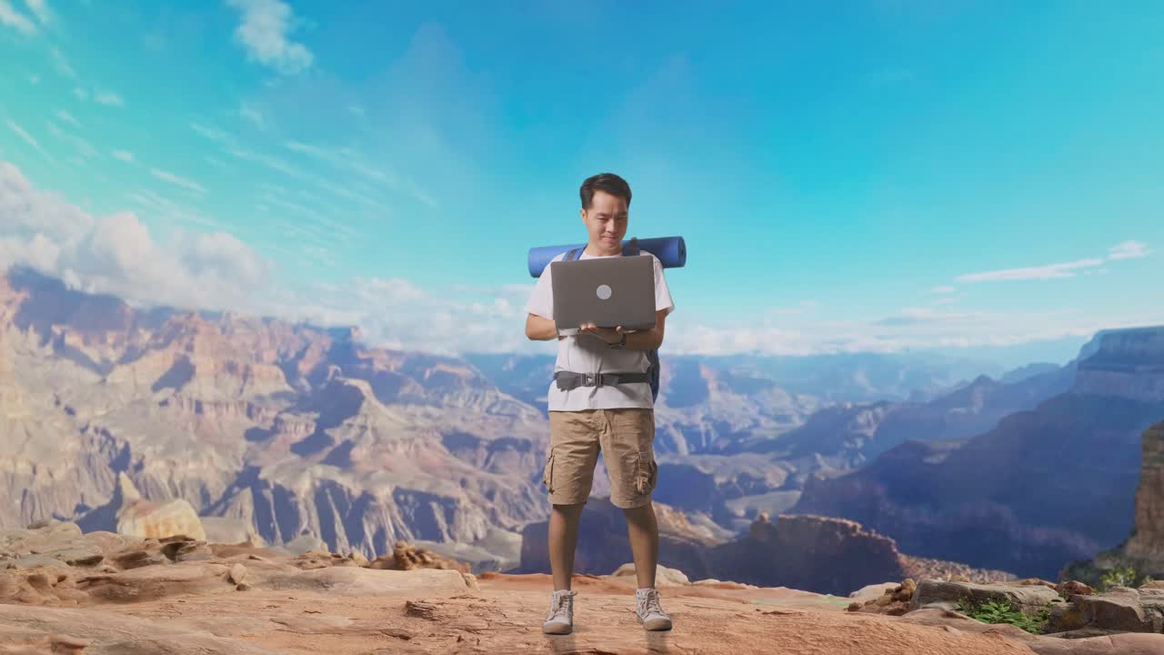 Full Body Of Asian Male Hiker With Mountaineering Backpack Using A Laptop While Traveling At The Top Of Mountain