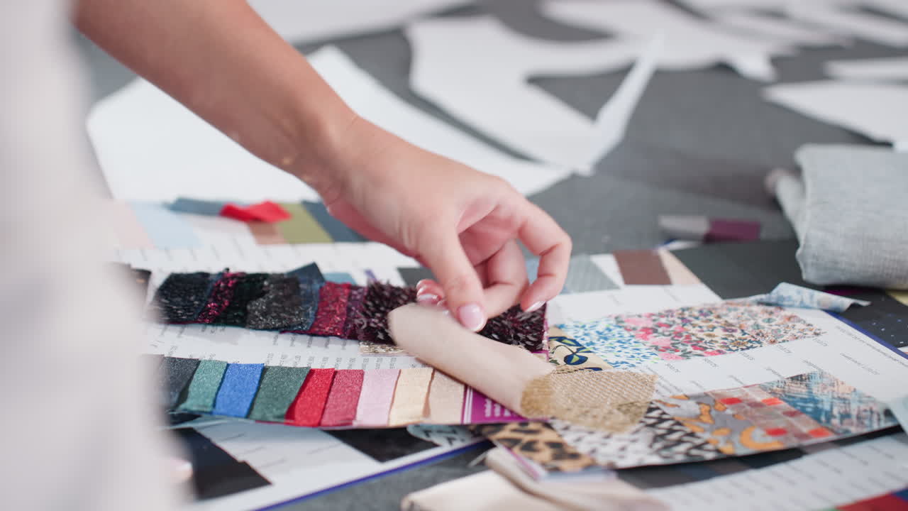 Close up of hand carefully lifting various colorful fabric samples during creative fabric selection process, showcasing vibrant materials, different textures, and fashion design development scene