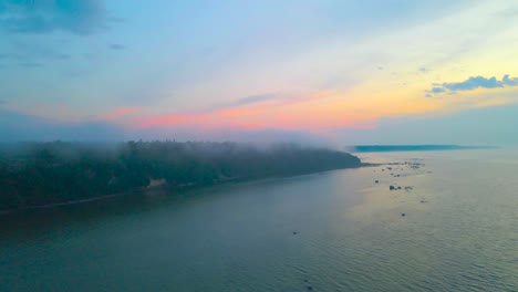 Aerial drone footage gliding and flying through clouds and mist and revealing a sunset ocean sea water shoreline with a steep cliff bank during orange and red vibrant sunset in Tabasalu Estonia Europe