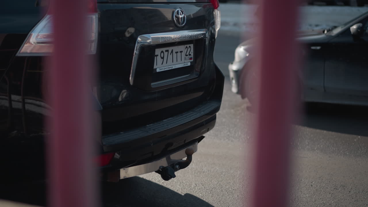 close up car headlight and bumper with mud flecks, suv parked on busy urban street as cars pass by on sunlit winter day, asphalt road, details, tow hitch, blur city background with motion reflections