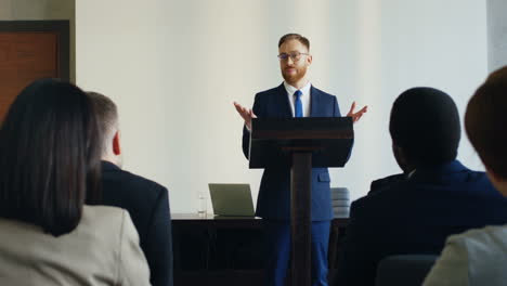 rear view of people sitting in a conference room who are listening to a caucasian businessman talking confidently and emotionally