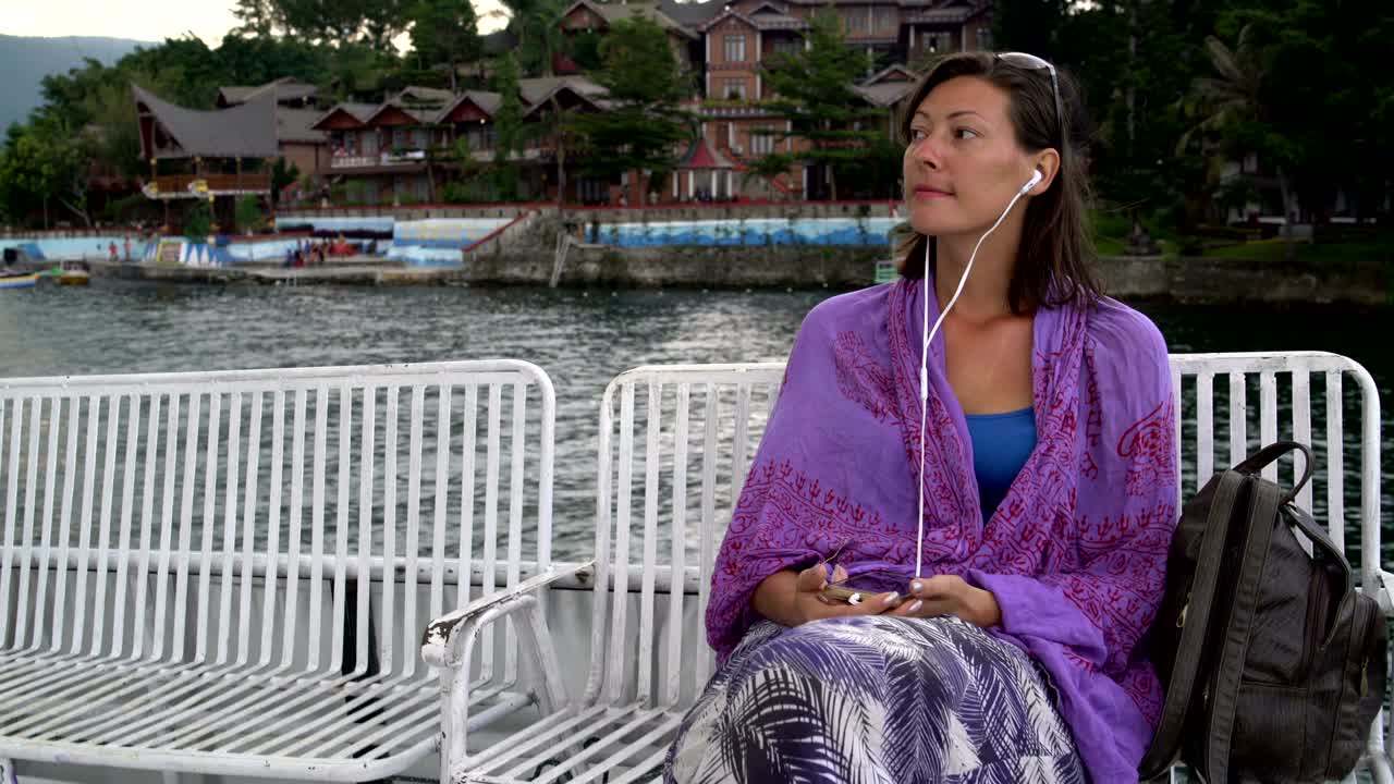 A woman sails on a boat and listens to music on headphones