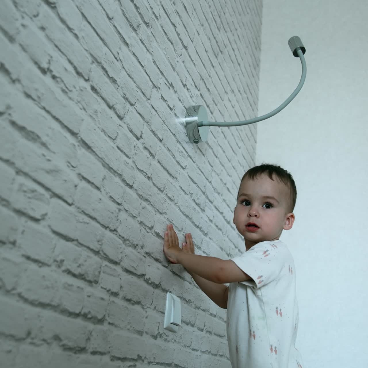 Happy active baby boy jumps excitedly on the bed. Kid plays with the lamp turning on and off the light. Low angle view