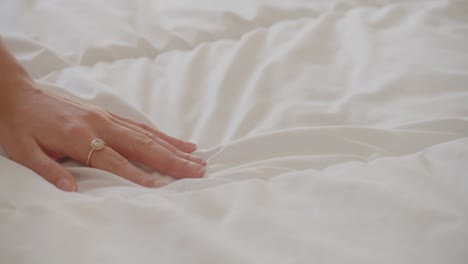 woman gently running her hand over bed sheet