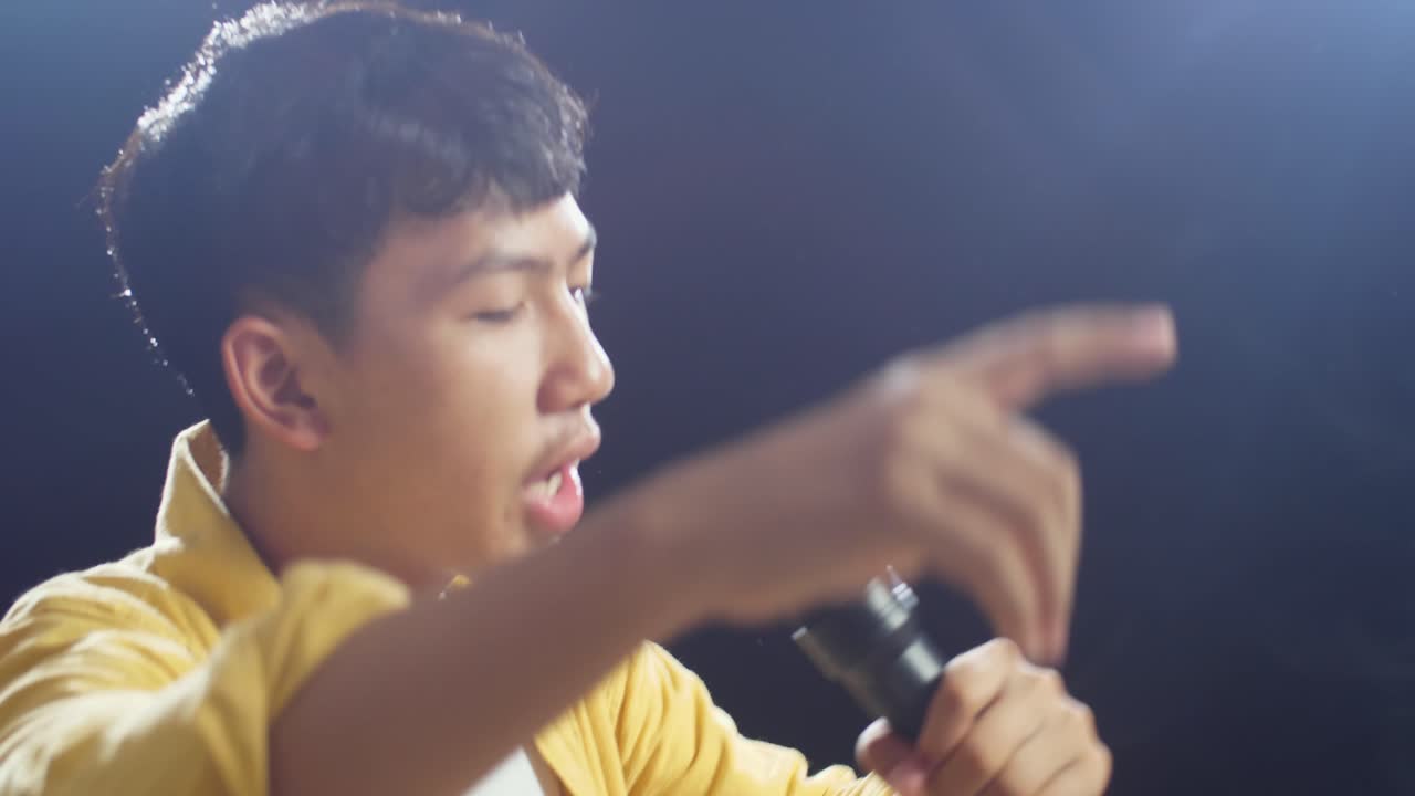 젊은 아시아 소년이 마이크를 들고 색 연기가 검은색 배경에 하는 가까운 측면 뷰