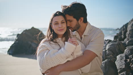 couple awaiting baby standing at sunny beach hugging closeup. family posing sea