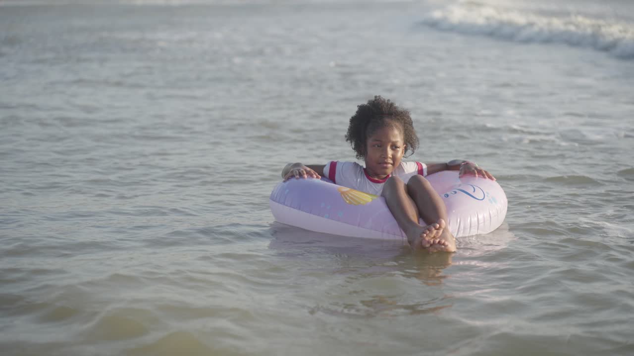 Happy Afro-American young girl smiling at beach, floating in sea with float
