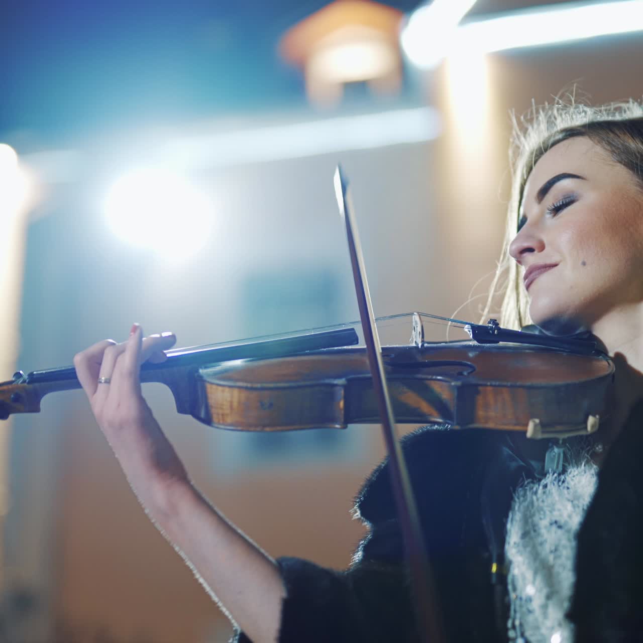 A creative girl in a black coat is playing the violin a romantic melody on the background of light from an evening lantern in the city. Close-up
