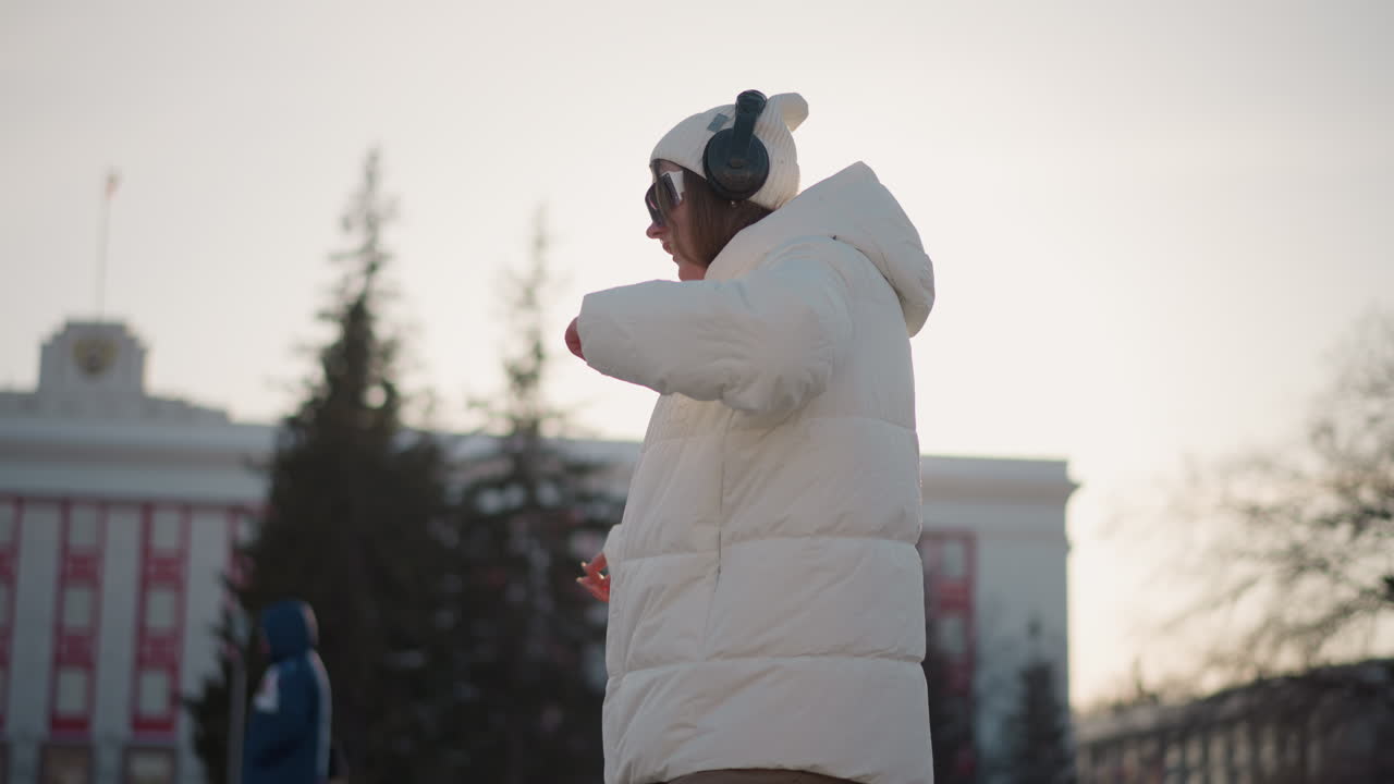 Radiant sunlight shines on free spirit dancing joyfully in winter attire, full of youthful spirit and graceful swaying motion, as warm glow creates serene atmosphere across snow-lined urban steps