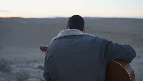 young man plays the guitar with beautiful desert background