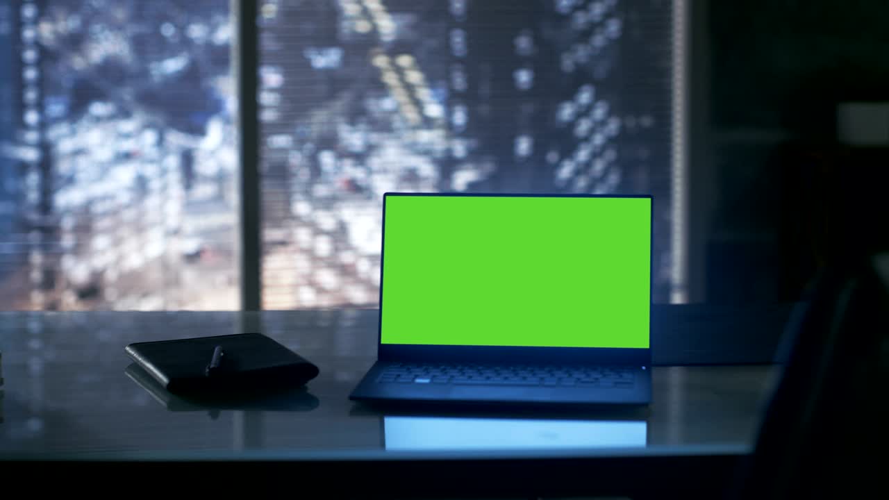 Close-up Footage of a Laptop with Green Mock-up Screen Standing on a Wooden Table. In the Background Big City Window View.
