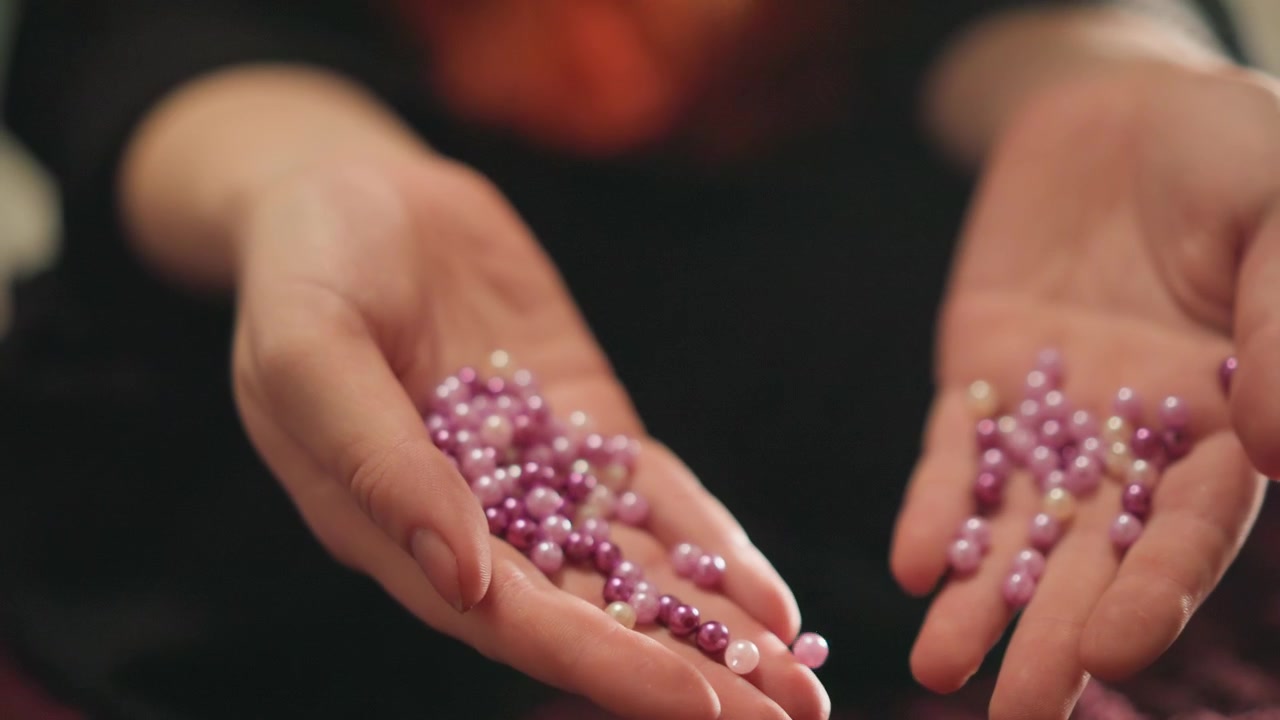 Mains caucasiennes ouvertes libérant des perles violettes sur du velours, déversement au ralenti, geste de reddition aux tons sombres, libération et clôture symboliques, bokeh cinématographique, ambiance mysticore, prévoyance émotionnelle.