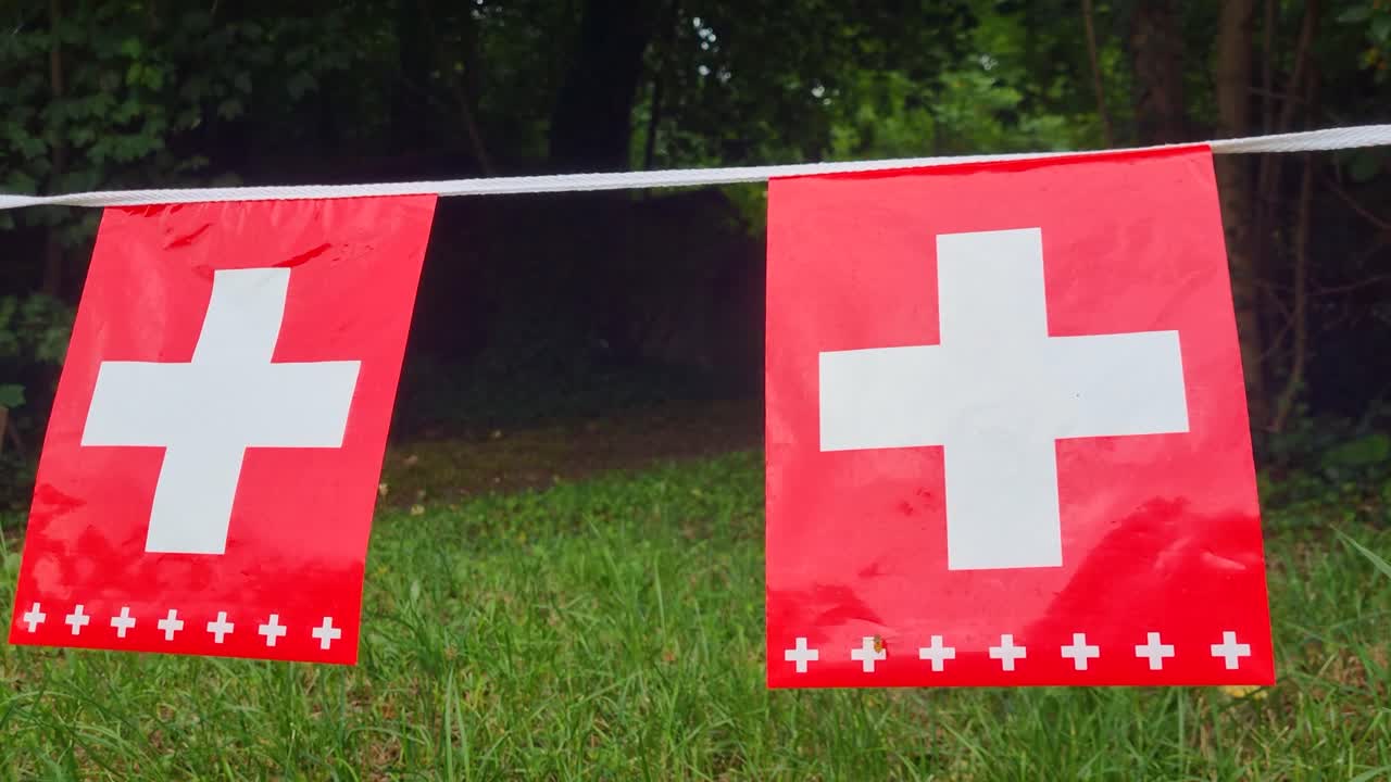 To små schweiziske flag hænger på en snor over en have, hvilket tilføjer festlig charme til Schweiz' nationaldagsfejringer