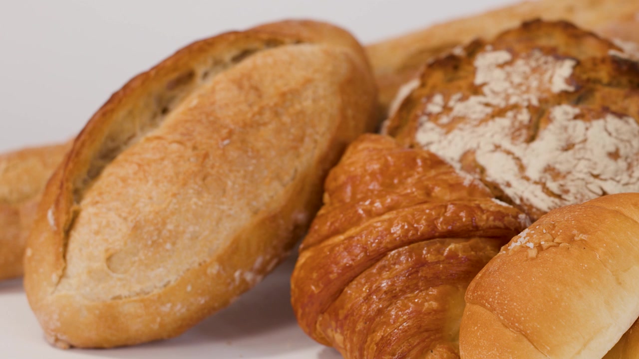 Primo piano di una mano che sistema pane a lievitazione naturale fresco, croissant e baguette su sfondo bianco da studio