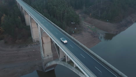 drone shot, white suv vehicle moving on bridge above river on dark cloudy autumn day