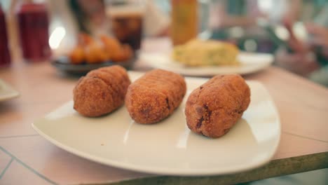 close up view of some traditional fried spanish croquetas (croquettes) appetizers served on a white plate placed on a rustic wooden table,