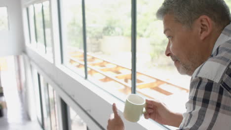 Thoughtful-senior-biracial-man-drinking-coffee-on-upstairs-landing-at-home,-copy-space,-slow-motion