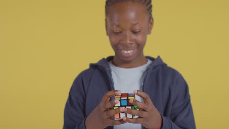 Studio-Portrait-Of-Young-Boy-On-ASD-Spectrum-Solving-Puzzle-Cube-On-Yellow-Background-2