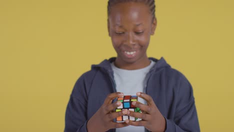 retrato de estudio de un niño en el espectro asd resolviendo un cubo de rompecabezas sobre fondo amarillo 2