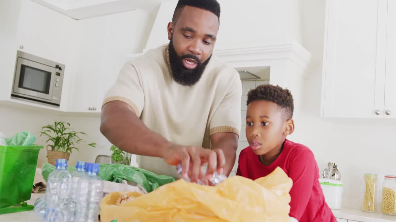 Happy african american father and son sorting waste in kitchen, in slow motion