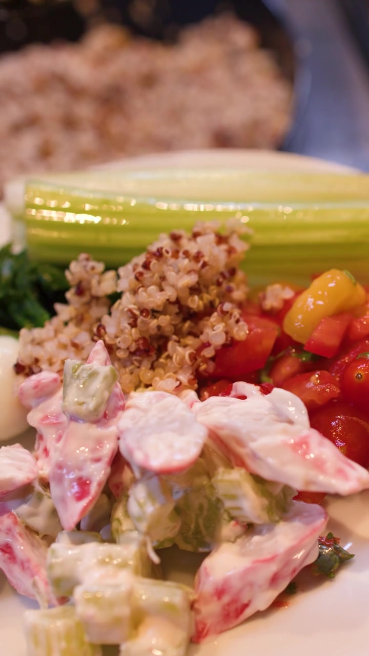 Un primo piano mostra un cucchiaio che serve quinoa cotta su un'insalata di verdure colorata.