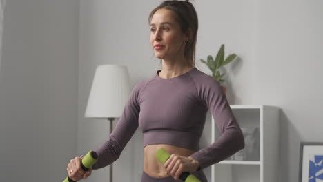 young-sporty-woman-is-moving-hands-with-dumbbells-to-sides-training-arms-muscular-at-home-fitness-in-apartment-medium-portrait-in-living-room