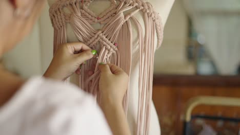 close-up of hands crafting a macrame garment on a mannequin