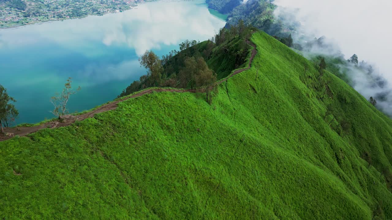 Trunyan Hill appears vibrant and green in aerial drone footage, as soft morning light spreads across the forested landscape with Lake Batur glistening in the distance.