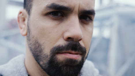 close-up view of the sweaty face of bearded sportsman during a training outdoors an abandoned factory on a cloudy morning