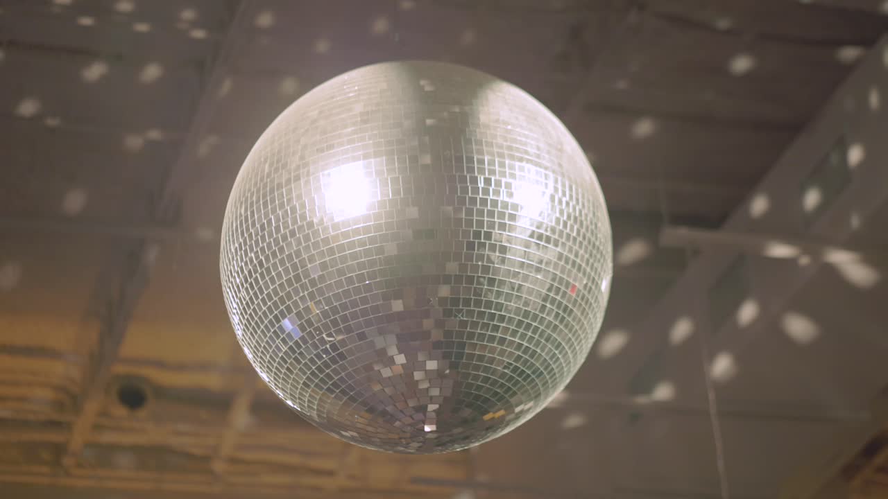 Una toma estable de una bola de discoteca brillante, girando, mientras cuelga de un techo, grabada a 60 fotogramas