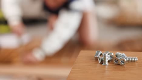 close-up of metal screws on a table with blurred background of furniture assembly in progress