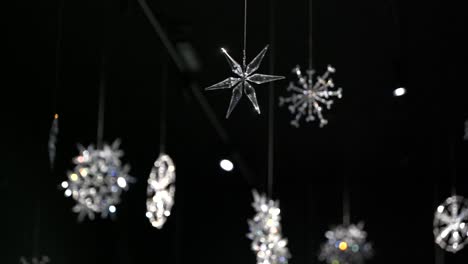 4k white sparkling crystal snowflakes hanging from the ceiling shining in the light and spinning slowly with black dark background