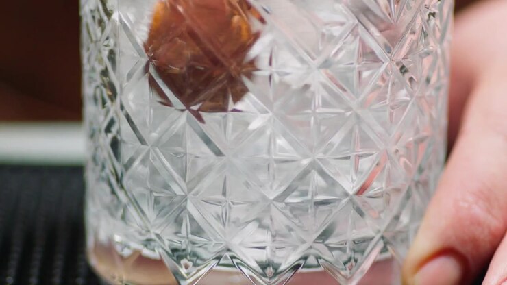 Ripresa in slow motion ravvicinata di un barman professionista che fa roteare cubetti di ghiaccio trasparenti all'interno di un bicchiere per raffreddarlo prima di preparare un cocktail artigianale in un bar di alto livello