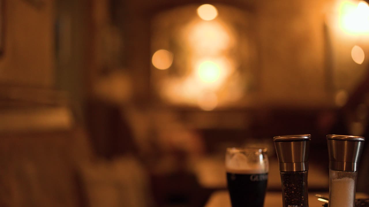 Dark beer glass and shakers on table, warm bokeh lighting, shallow focus, pub interior