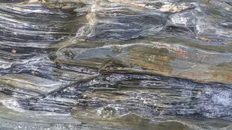 Natural-grey-and-green-stone-closeup-being-washed-by-the-natural-sea-waves,-Elba-island---Italy